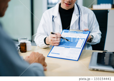 Asian doctor points to a medical form while consulting a patient in a bright clinic office. Concept of health care, insurance 133154441