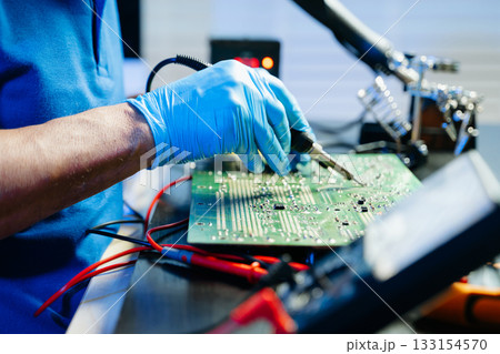 Closeup of expert soldering a green PCB board using precision tools. Ideal for electronics, circuit repair, engineering, tech Closeup of expert soldering a green PCB board using precision tools. Ideal for electronics, circuit repair, engineering, tech 133154570
