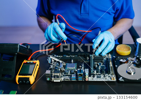 Technician uses multimeter on motherboard for diagnostics. Gloves, tools, and hardware setup show real people Technician uses multimeter on motherboard for diagnostics. Gloves, tools, and hardware setup show real people 133154600