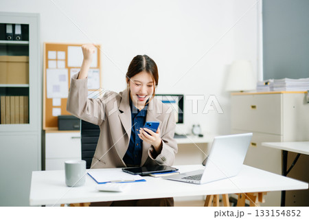businesswoman celebrating success at her desk with laptop and tablet in a modern office. Perfect for themes of victory, achievement, productivity 133154852