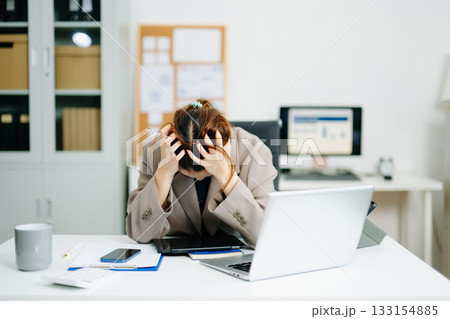 Young woman overwhelmed and exhausted at her desk in modern office. Struggling with stress, deadlines, and data reports. Young woman overwhelmed and exhausted at her desk in modern office. Struggling with stress, deadlines, and data reports. 133154885