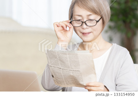 リビングで老眼鏡をかけて新聞を読むシニア女性 133154950