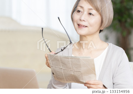 リビングで老眼鏡をかけて新聞を読むシニア女性 133154956