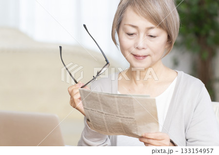 リビングで老眼鏡をかけて新聞を読むシニア女性 133154957