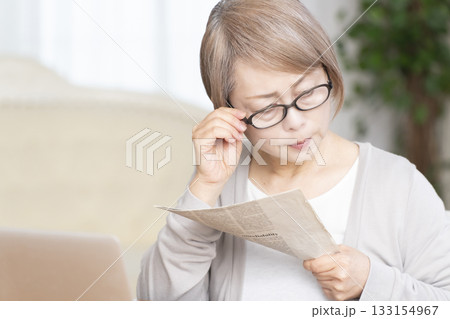 リビングで老眼鏡をかけて新聞を読むシニア女性 133154967
