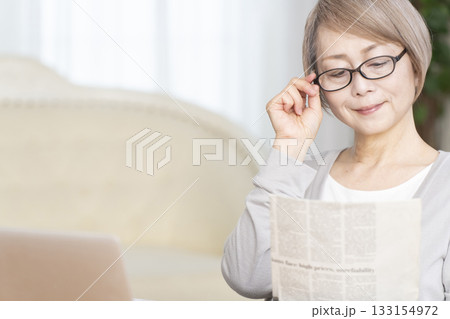 リビングで老眼鏡をかけて新聞を読むシニア女性 133154972