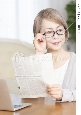 リビングで老眼鏡をかけて新聞を読むシニア女性 133154977