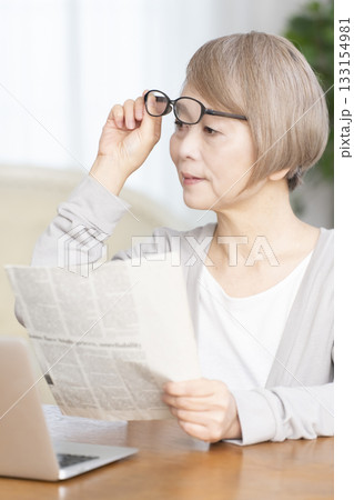 リビングで老眼鏡をかけて新聞を読むシニア女性 133154981