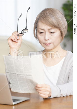 リビングで老眼鏡をかけて新聞を読むシニア女性 133154985