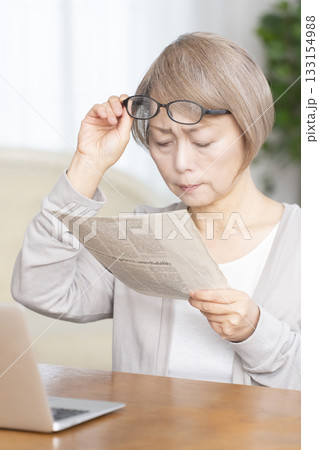 リビングで老眼鏡をかけて新聞を読むシニア女性 133154988
