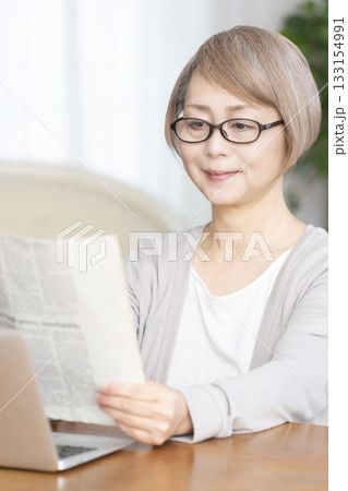 リビングで老眼鏡をかけて新聞を読むシニア女性 リビングで老眼鏡をかけて新聞を読むシニア女性 133154991