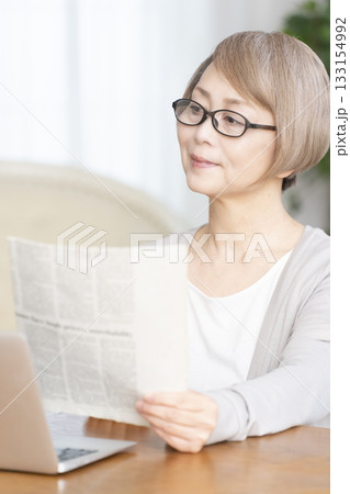 リビングで老眼鏡をかけて新聞を読むシニア女性 リビングで老眼鏡をかけて新聞を読むシニア女性 133154992