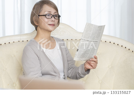 リビングのソファーに座り老眼鏡をかけて新聞を読むシニア女性 リビングのソファーに座り老眼鏡をかけて新聞を読むシニア女性 133155027