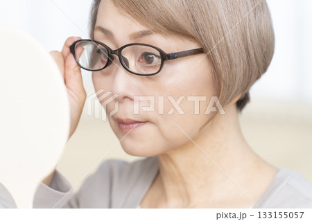 リビングで老眼鏡をかけて手鏡を見るシニア女性 133155057
