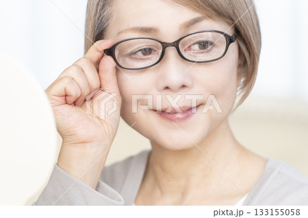 リビングで老眼鏡をかけて手鏡を見るシニア女性 133155058