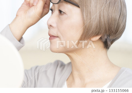 リビングで老眼鏡をかけて手鏡を見るシニア女性 133155066