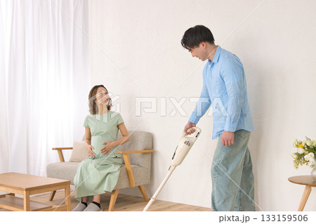 妊婦の女性と話しながら楽しそうに掃除機をかける若い男性 133159506