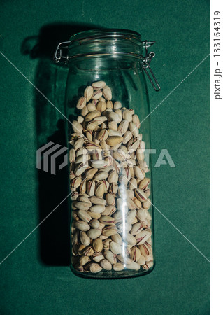 Salted pistachios with glass jar green background Salted pistachios with glass jar green background 133164319