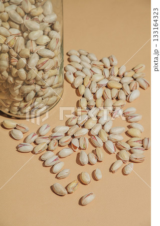 Salted pistachios in their shells alongside a glass container 133164323