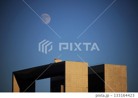 夕暮れ時幾何学的なビルの上に浮かび上がる月 夕暮れ時幾何学的なビルの上に浮かび上がる月 133164423