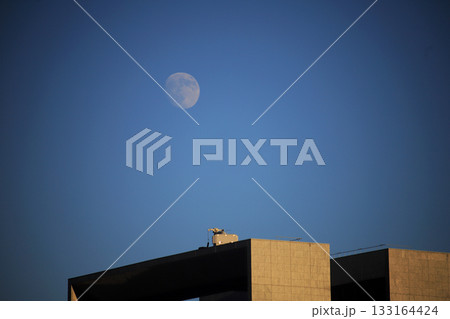 夕暮れ時幾何学的なビルの上に浮かび上がる月 133164424