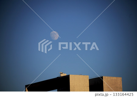 夕暮れ時幾何学的なビルの上に浮かび上がる月 133164425