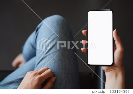 Young woman hold smarphone with white screen while sitting in a chair Young woman hold smarphone with white screen while sitting in a chair 133164595