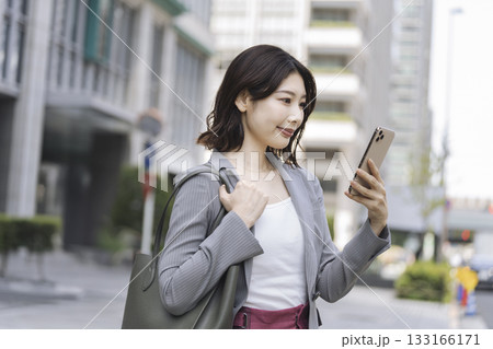 オフィス街でスマートフォンの画面を見るビジネスウーマン 133166171