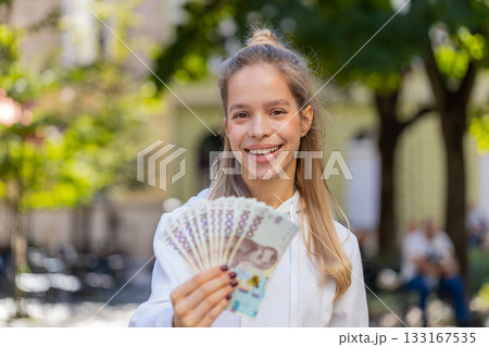 Happy Caucasian young woman girl holding fan of euro showing thumbs up gesture on city street 133167535