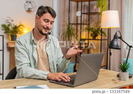 Young male customer service representative with headset using laptop computer at home office table Young male customer service representative with headset using laptop computer at home office table 133167589