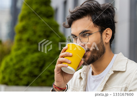 Happy Indian man enjoying drinking morning coffee hot drink, relaxing, taking a break in city street Happy Indian man enjoying drinking morning coffee hot drink, relaxing, taking a break in city street 133167600