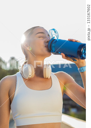 Athletic fit sport runner girl woman drinking water from bottle after training exercise in park 133167602