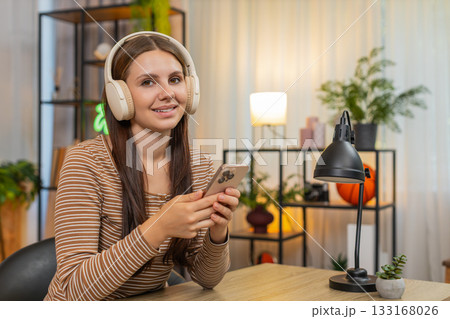 Young woman in headphones listens to work podcast saves ideas to notes on smartphone while focused Young woman in headphones listens to work podcast saves ideas to notes on smartphone while focused 133168026