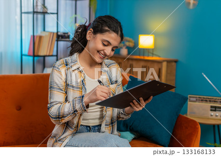 Indian woman carefully reading documents contract on tablet writing notes with pen serious focused Indian woman carefully reading documents contract on tablet writing notes with pen serious focused 133168133