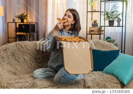 Happy young Caucasian woman receives delivery box unpacks it and enjoys delicious pizza at home Happy young Caucasian woman receives delivery box unpacks it and enjoys delicious pizza at home 133168160