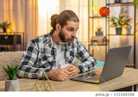 Young man browsing laptop shop at home, coffee by side, exclaim wow, huge discount, joyful surprise Young man browsing laptop shop at home, coffee by side, exclaim wow, huge discount, joyful surprise 133168166
