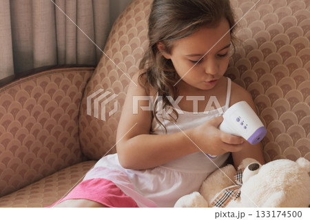 Learning care: child practices health monitoring skills on her bear with a digital thermometer 133174500