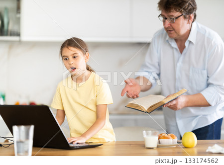 Father offers to read book to his daughter while she uses laptop 133174562