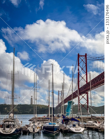 Several sailing boats anchored below famous red April 25th or 25 de Abril bridge in Lisbon, Portugal in river Tejo or Tagus estuary. Fluffy clouds in blue sky on sunny day, monument to Christ the King Several sailing boats anchored below famous red April 25th or 25 de Abril bridge in Lisbon, Portugal in river Tejo or Tagus estuary. Fluffy clouds in blue sky on sunny day, monument to Christ the King 133176496