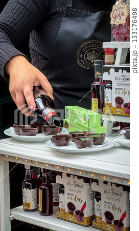 Obidos, Portugal - Dec 30, 2023: Female hand pouring traditional Portuguese ginja liqueur into edible chocolate cups, sweet cherry drink, popular local specialty and tourist souvenir. Authentic Obidos, Portugal - Dec 30, 2023: Female hand pouring traditional Portuguese ginja liqueur into edible chocolate cups, sweet cherry drink, popular local specialty and tourist souvenir. Authentic 133176498