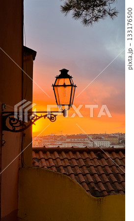 Beautiful view in shades of red and orange of colorful sunset over historic buildings and antique original street lamp against vibrant cloudy sky. European tile rooftops, historic scene at dusk Beautiful view in shades of red and orange of colorful sunset over historic buildings and antique original street lamp against vibrant cloudy sky. European tile rooftops, historic scene at dusk 133176500