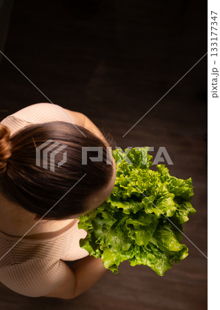 Woman Holds Fresh Green Lettuce Against Dark Background 133177347