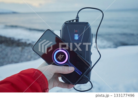 Charging a smartphone from a power bank against the backdrop of the sea and snow in winter 133177496