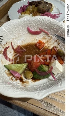 Half-eaten greek salad on ornate white plate with cucumbers, tomatoes, feta, and olives Half-eaten greek salad on ornate white plate with cucumbers, tomatoes, feta, and olives 133179862