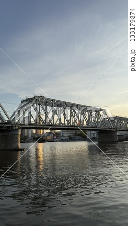 City bridge over calm river at sunset reflecting in water with an urban skyline in background 133179874