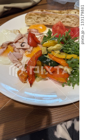 Breakfast plate with fried eggs, bacon, grilled vegetables, tomato, arugula, and bread 133179881