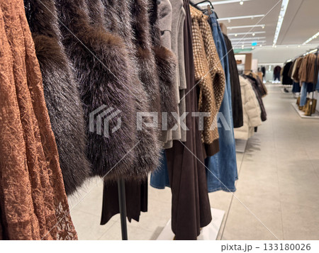 A row of warm autumn and winter clothing, including faux fur, knits, and textures, hangs neatly in a store A row of warm autumn and winter clothing, including faux fur, knits, and textures, hangs neatly in a store 133180026