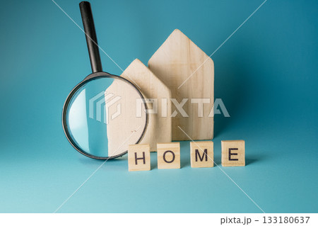 Wooden house shapes and magnifying glass with letter blocks spelling home on blue background 133180637