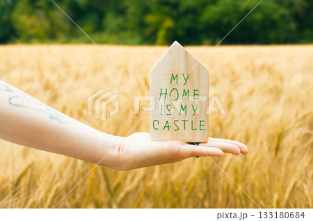 Hand holding a wooden house sign that says My home is my castle. Hand holding a wooden house sign that says My home is my castle. 133180684
