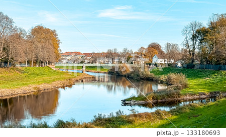 Serene river landscape with lush greenery and autumn foliage under a clear blue sky Serene river landscape with lush greenery and autumn foliage under a clear blue sky 133180693